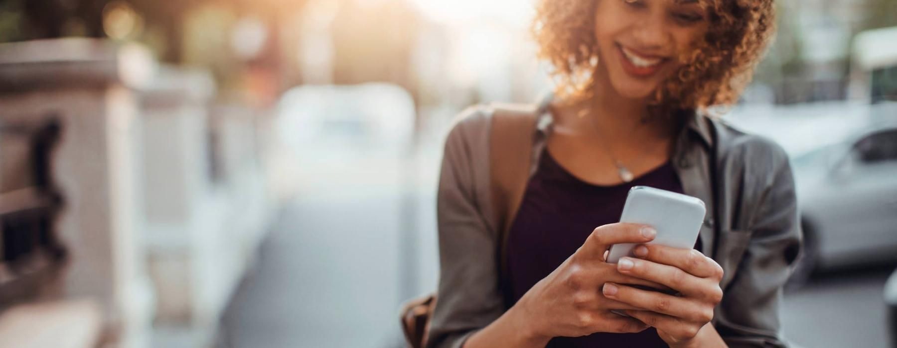 woman texts on her phone as she walks through the city